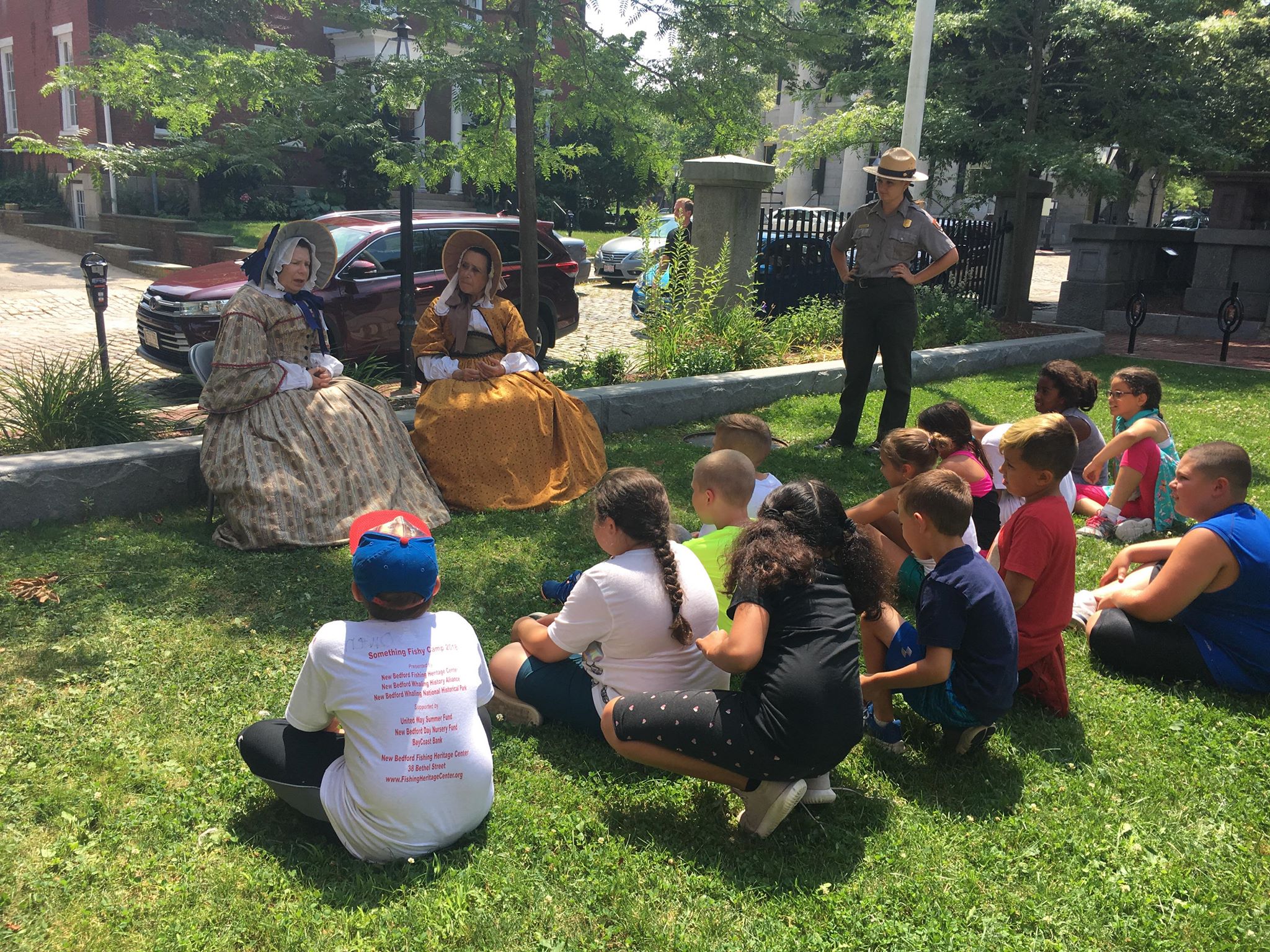 Two women dressed in 1850s clothes speak to a group of youths