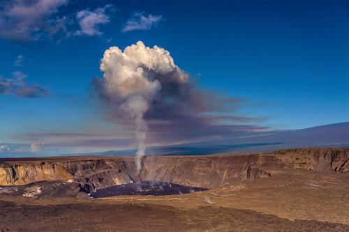 A volcanic crater producing lava from a cone with a large mushroom shaped volcanic plume above it. 