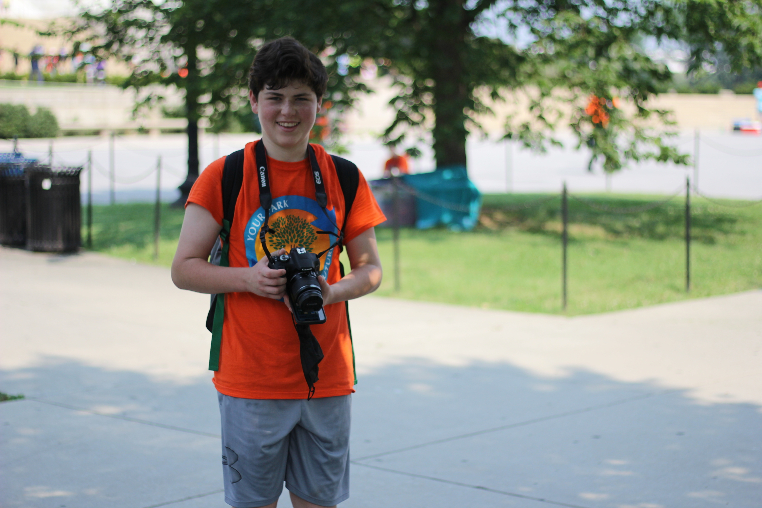 President's Park student volunteer,  Eli Schwartz smiles while holding a camera around his neck. 