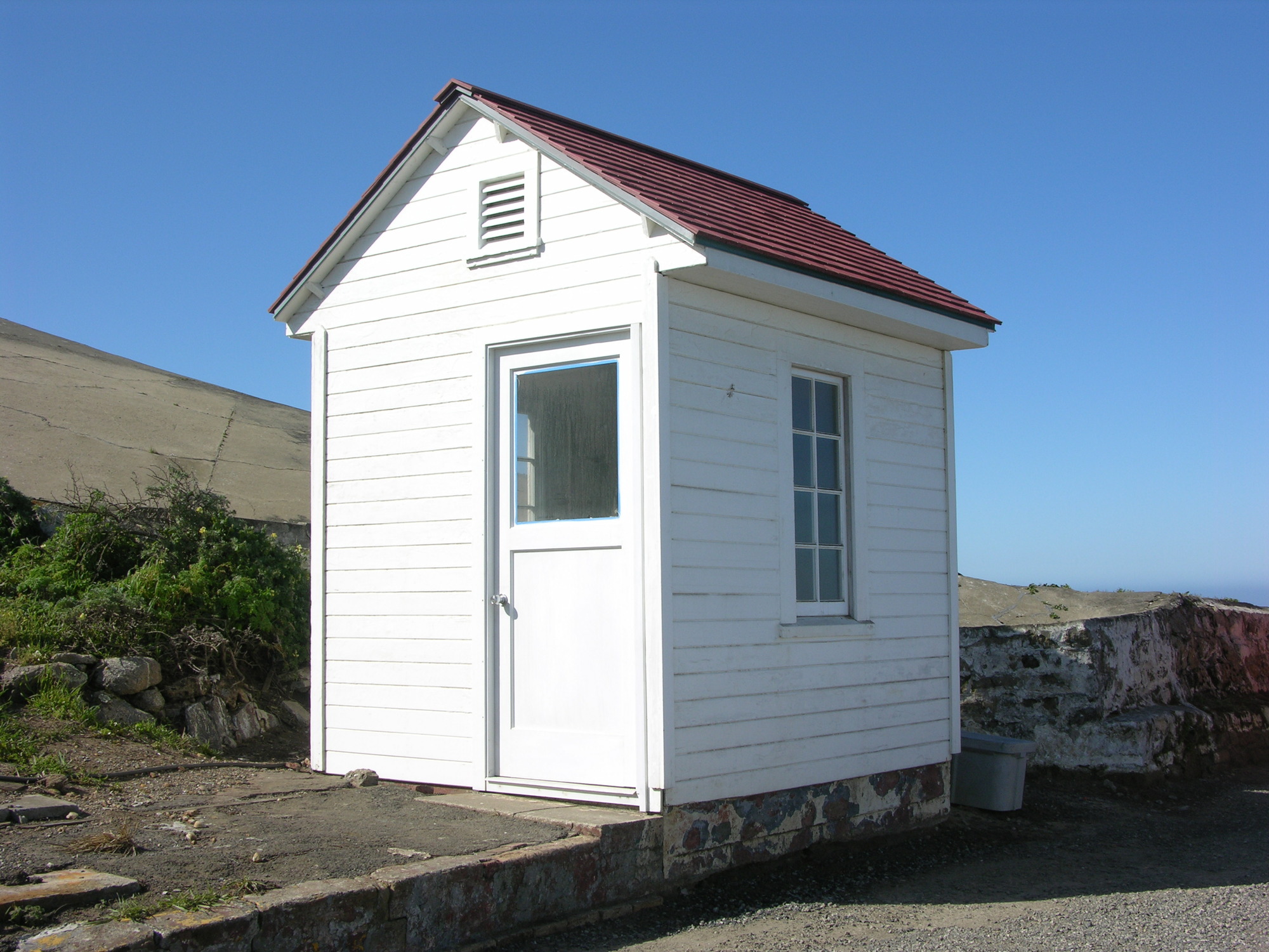 A small white-sided and red-roofed building has a new door and windows.