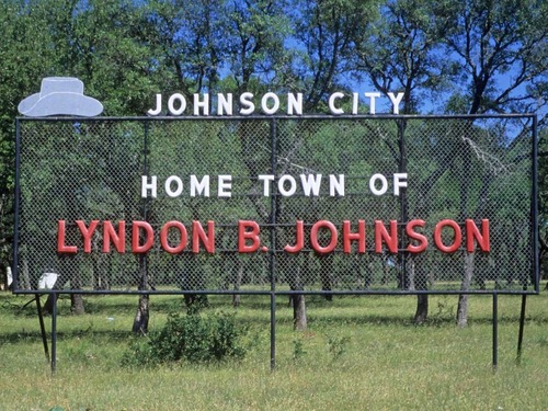 A large mesh metal sign. In white letters it reads "Johnson City, Home Town of," and then in red letters, "Lyndon B. Johnson." A two-dimensional illustration of a cowboy hat sits on the top, right corner.