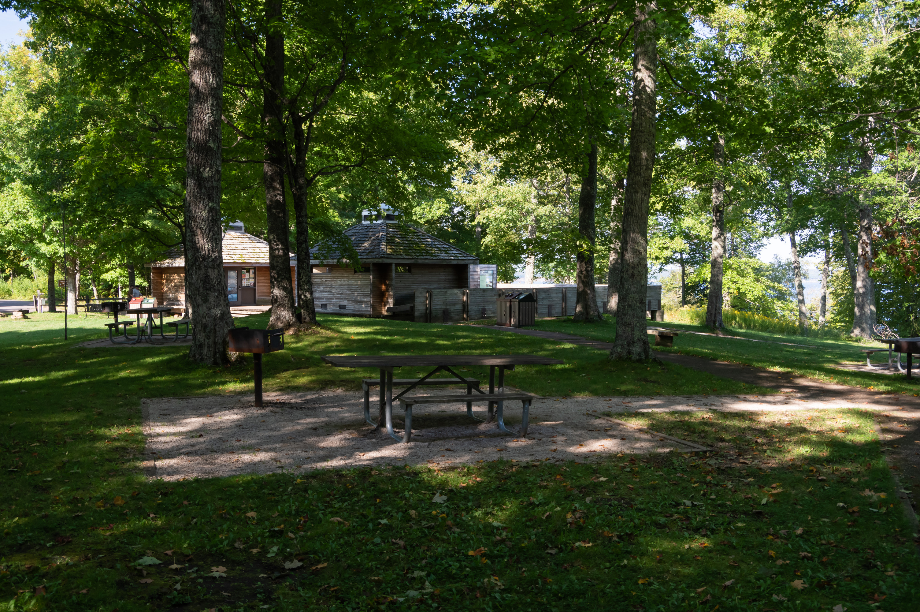 Picnic tables in the shade. Restroom facilities are in the background.