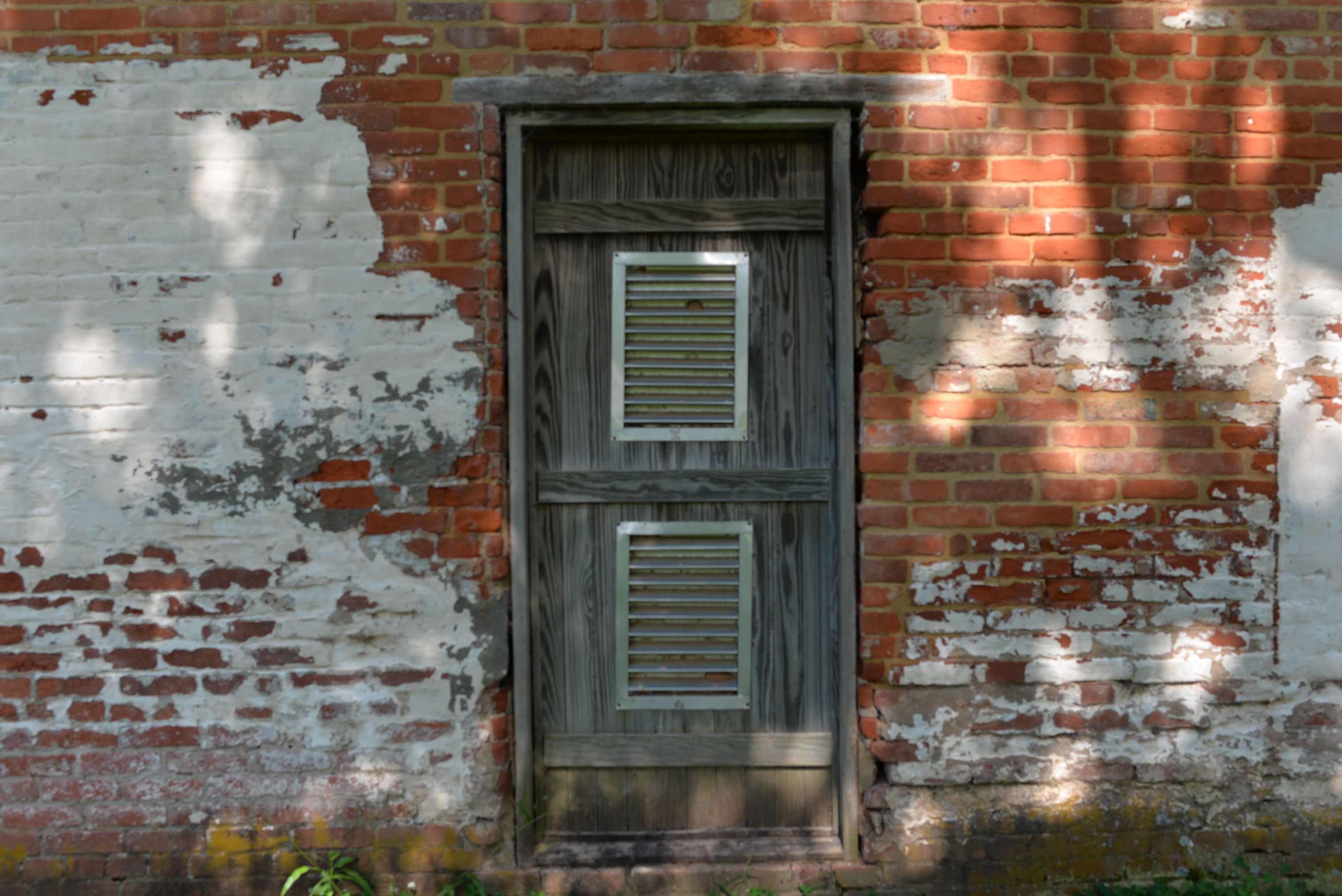Closeup view of wooden door with metal slates to a brick structure.