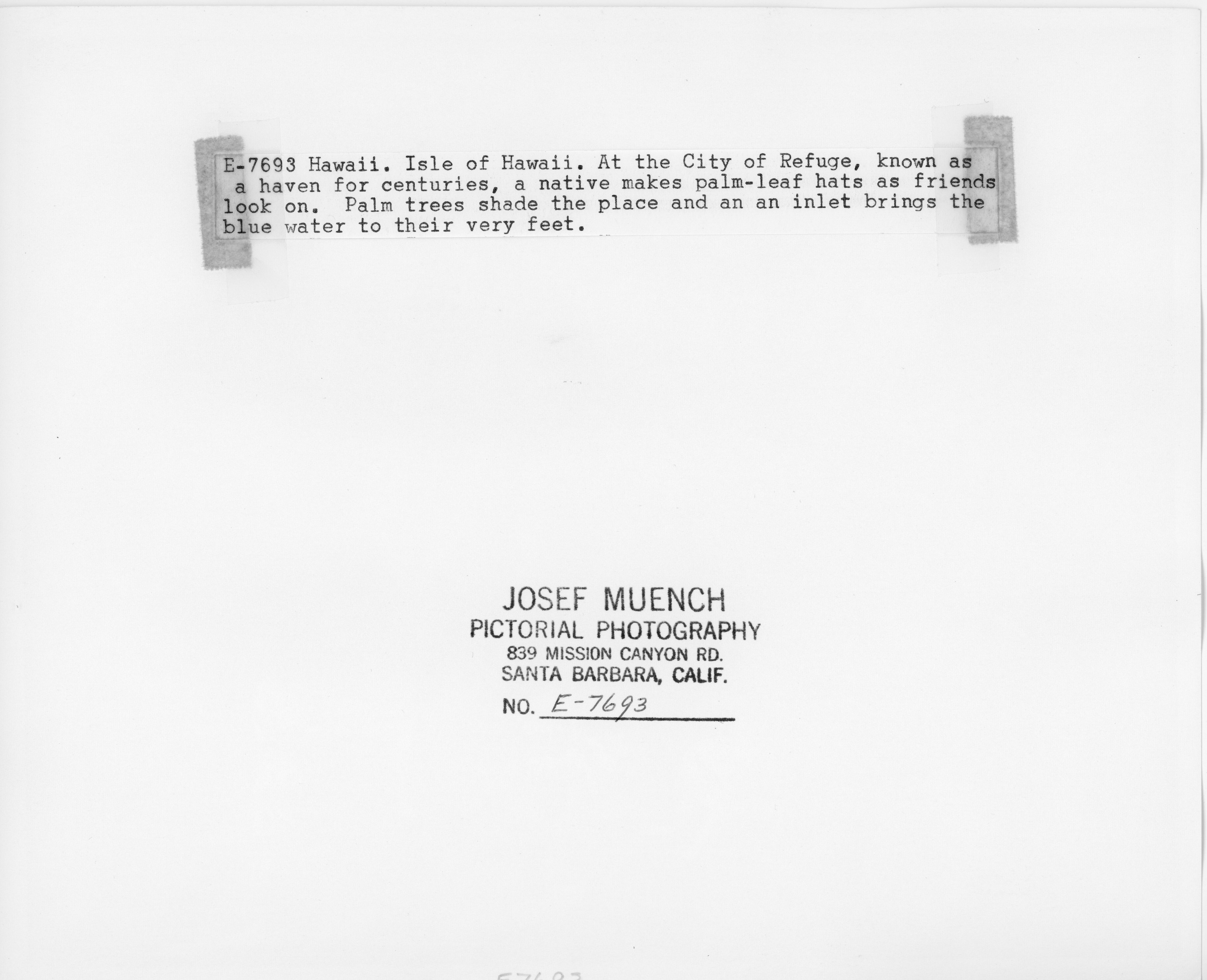 The back of an image of four people observing hat weaving near the bay. There is text on the back of the image that reads, “E-5693 Hawaii. Isle of Hawaii. At the City of Refuge, known as a haven for centuries, a native makes palm-leaf hats as friends look on. Palm trees shade the place and an inlet brings the blue water to their very feet." At the bottom, it has the photographer's name, “Josef Muench,” where the image was produced, “Pictorial Photography, 839 Mission Canyon Road. Santa Barbara, California.," and the number assigned to the image, "E-7693."
