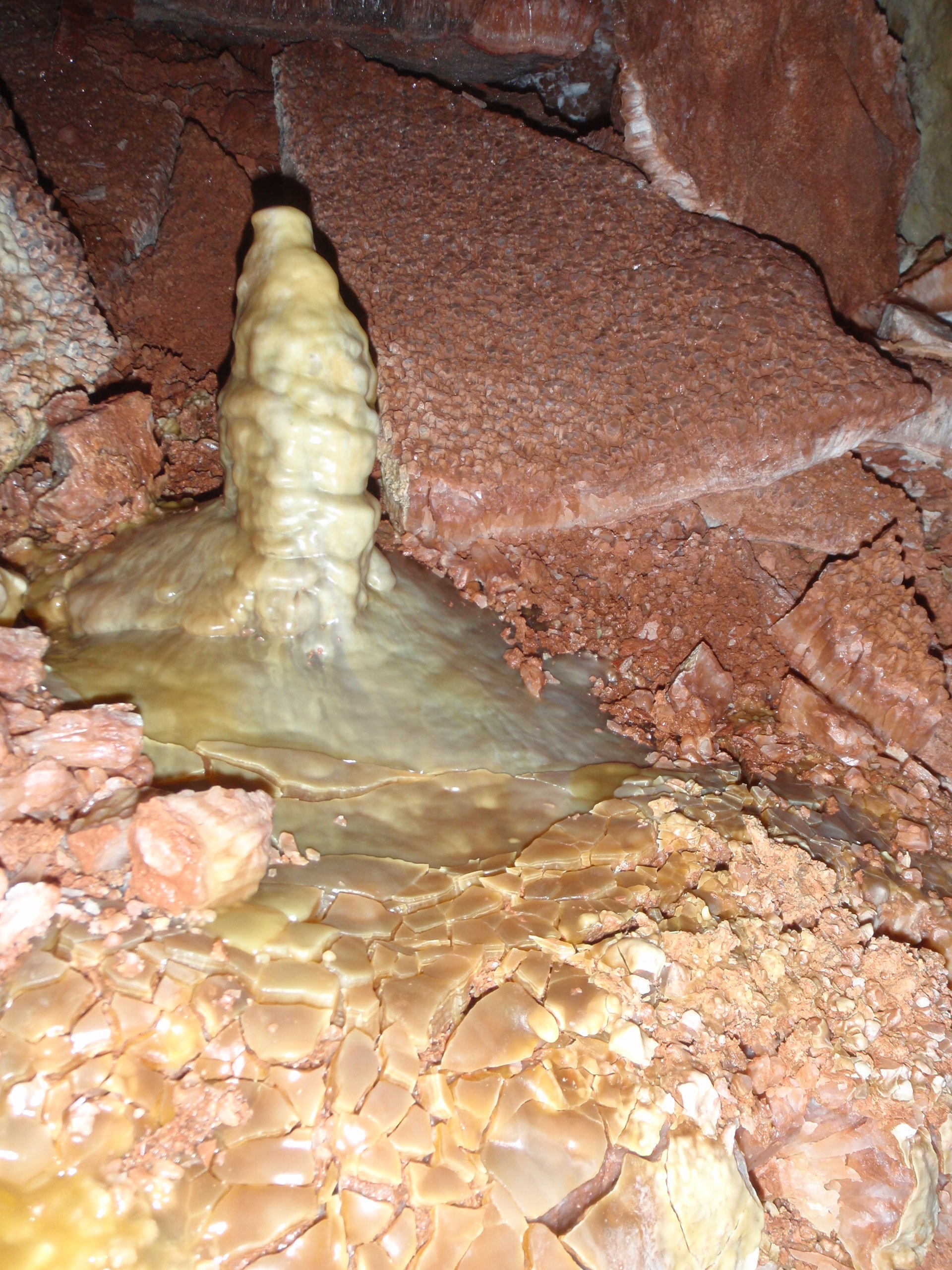 A stalagmite on the ground with reddish calcite crystal breakdown in background