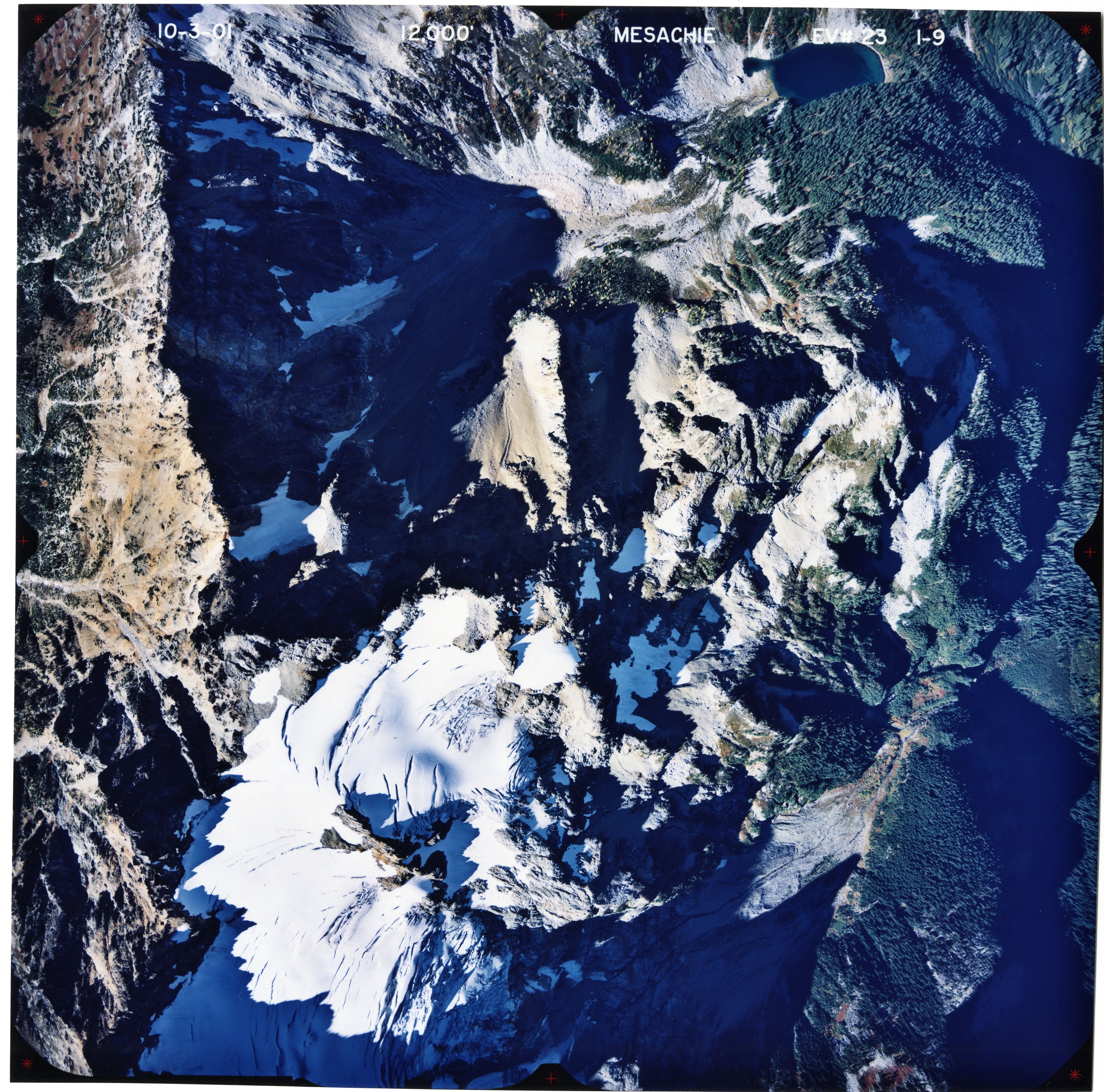 Color aerial photograph of glaciated mountain peak with forested valleys below.