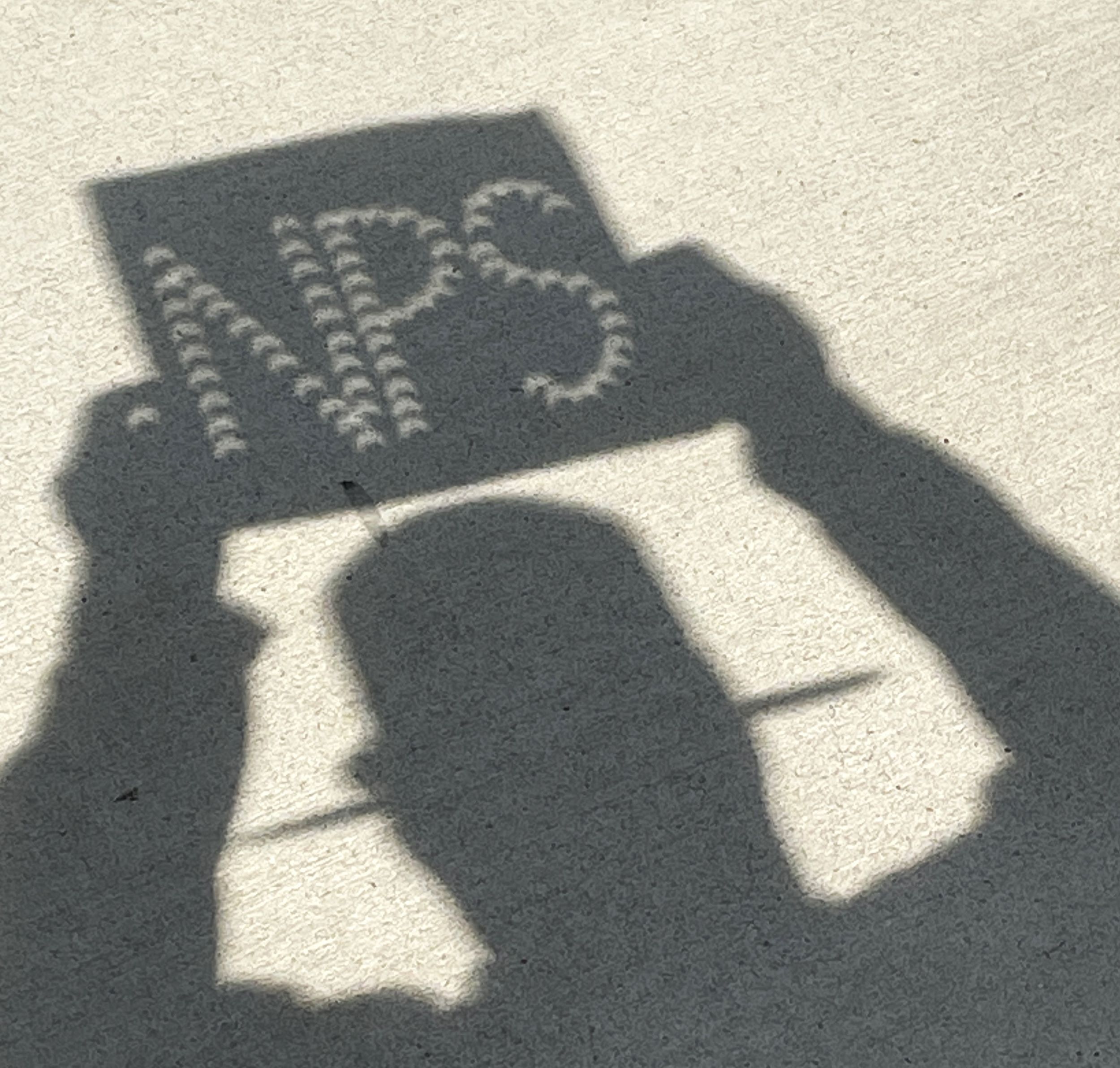 Crescent sun shadows shine through an NPS sign during the partial eclipse