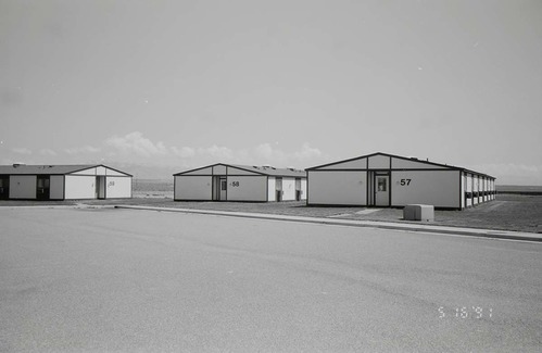 Barracks and parking area. Building numbers 57, 58, and 59. Mountains in background. [Image possibly for comparative housing study]