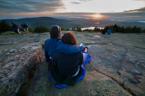 A couple sits on rock looking out at a sunrise