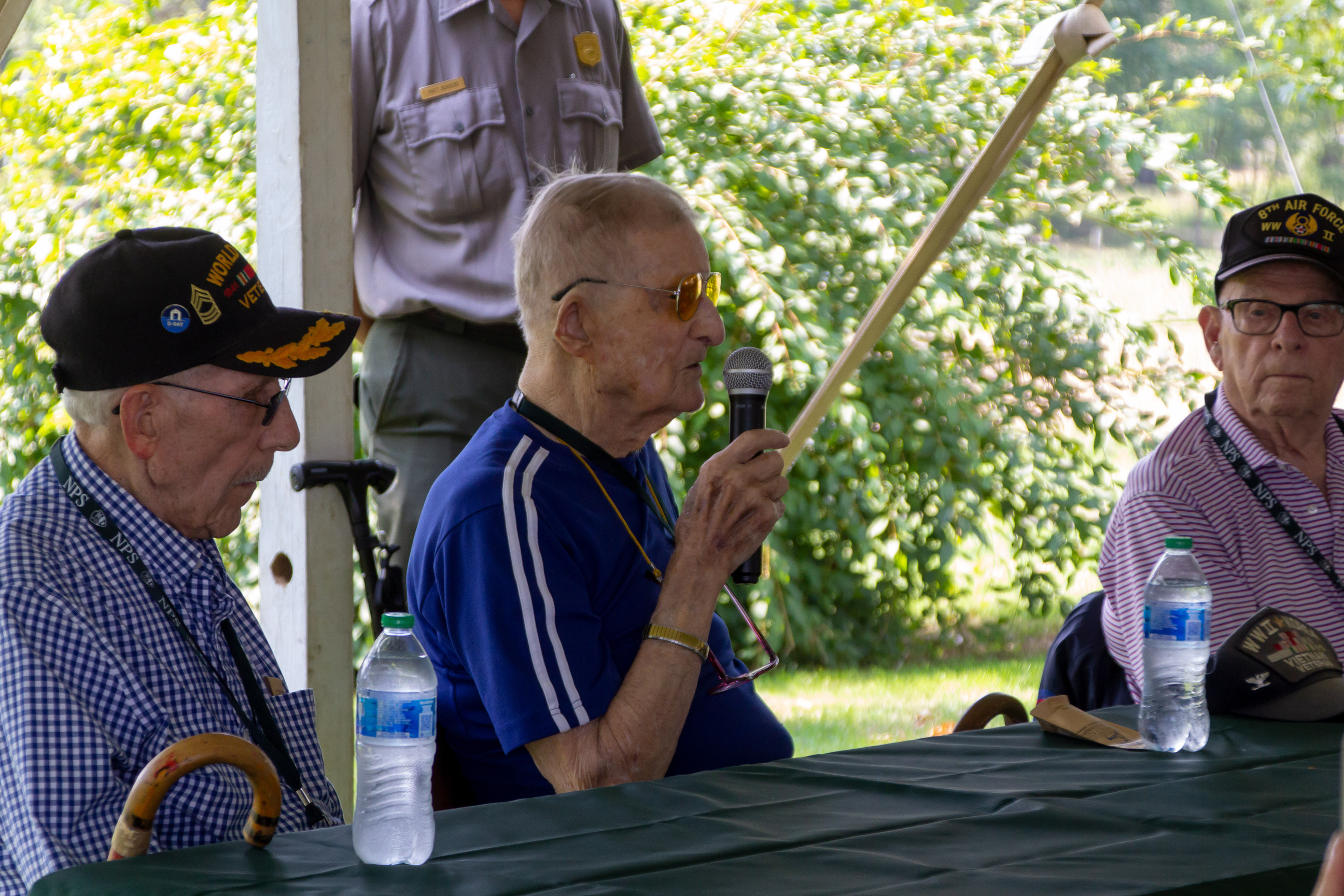 A World War 2 veteran talks with a microphone under a tent.