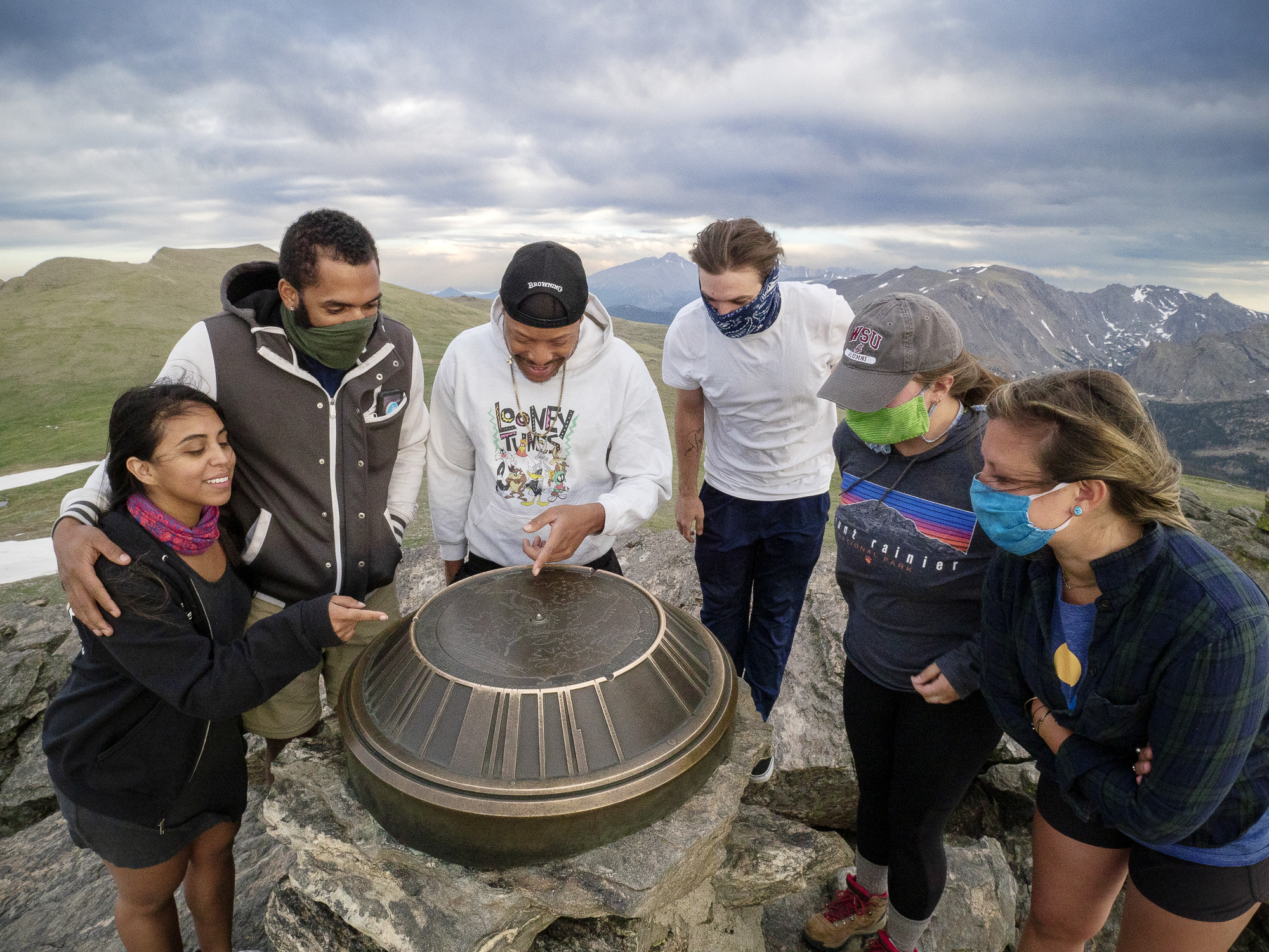 six people point to different points on a large metal disk