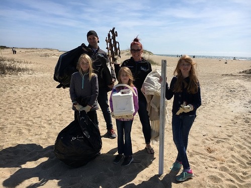 Photo of family holding different pieces of trash picked up during a beach cleanup event.