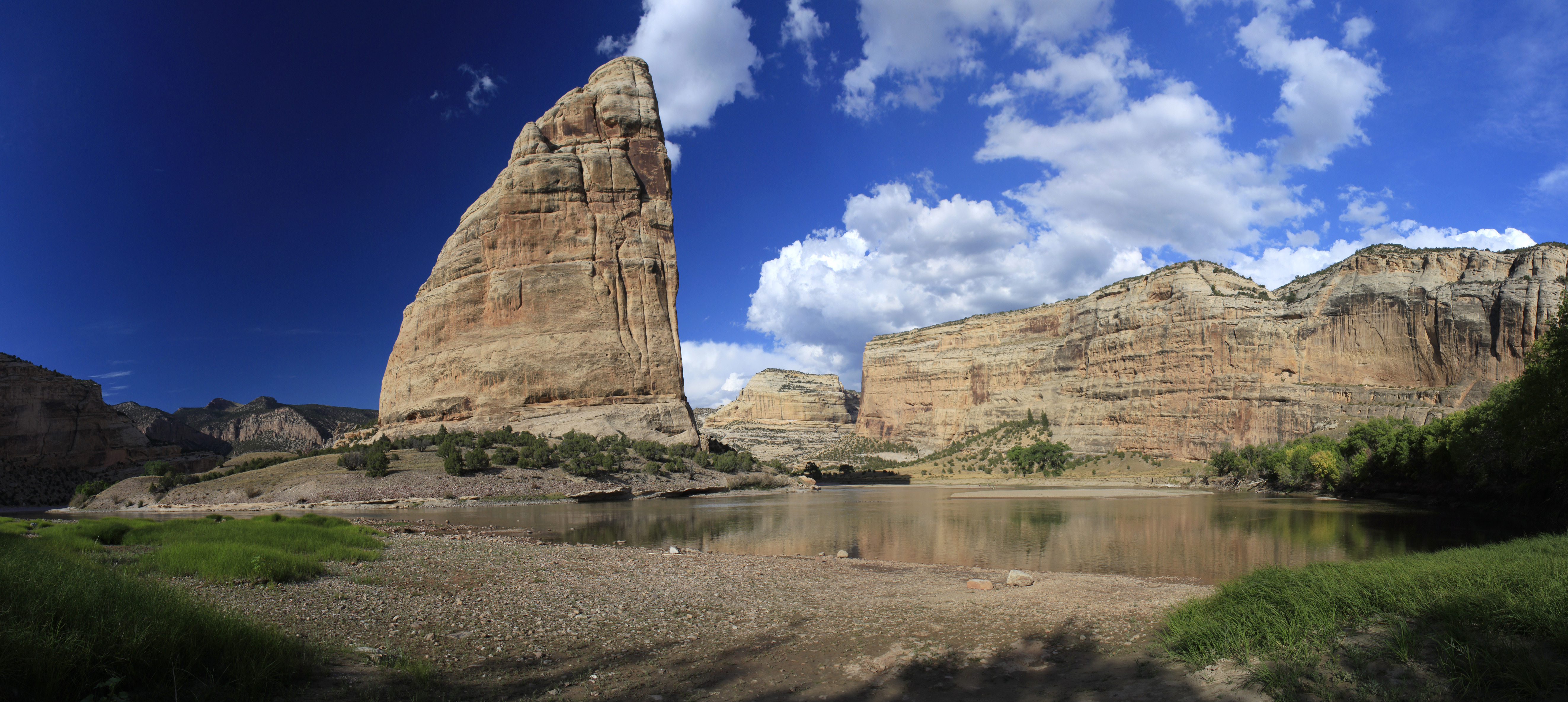 A large rock monolith and tan cliffs rise above a placid river