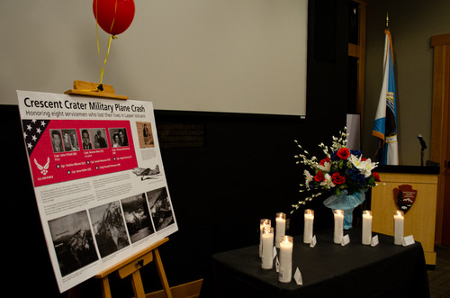 A display rests on a wooden easel adjacent to a table with eight candles to honor eight servicemen who lost their lives in a 1951 airplane crash on Crescent Crater.