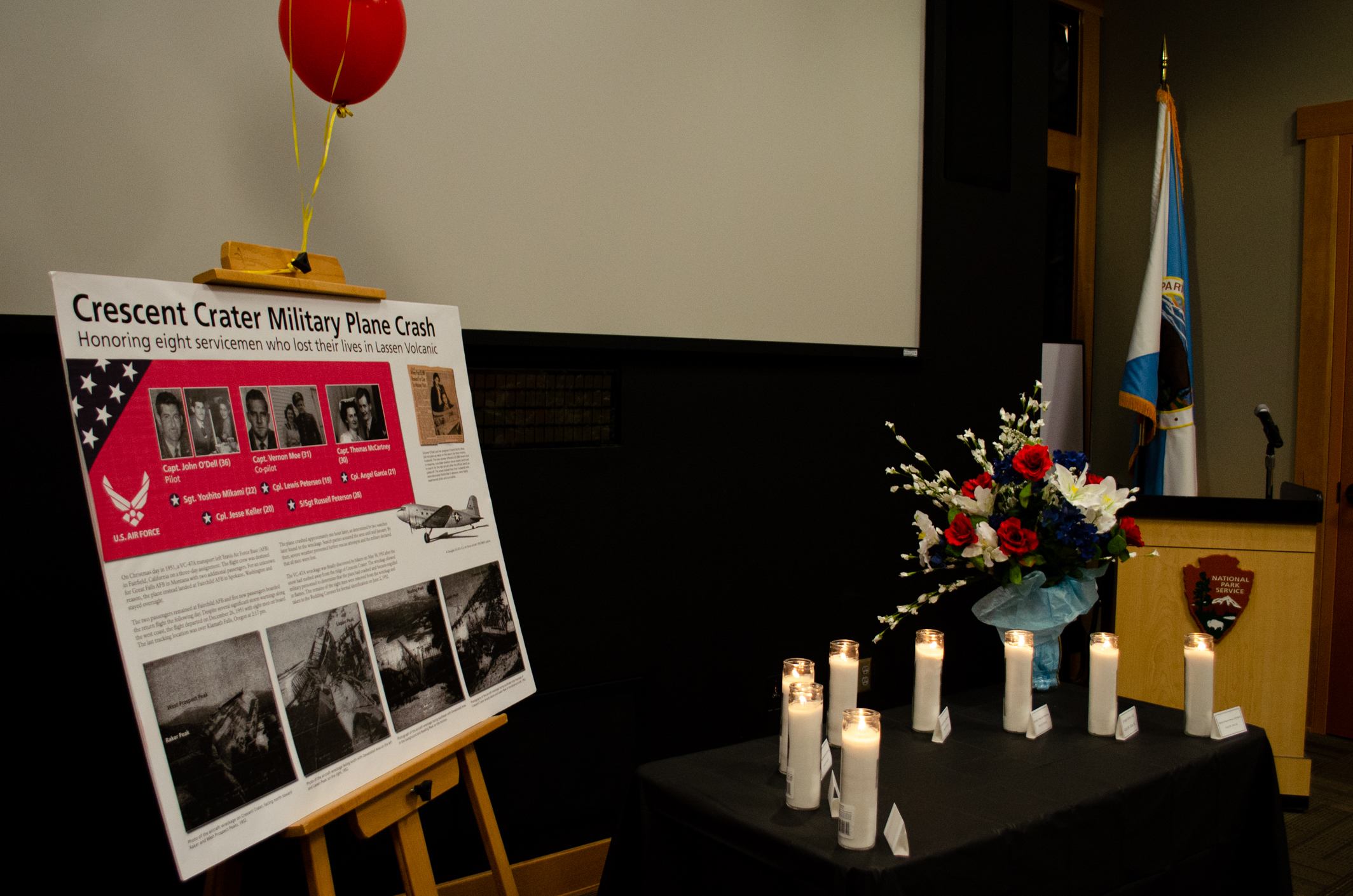 A display rests on a wooden easel adjacent to a table with eight candles to honor eight servicemen who lost their lives in a 1951 airplane crash on Crescent Crater.