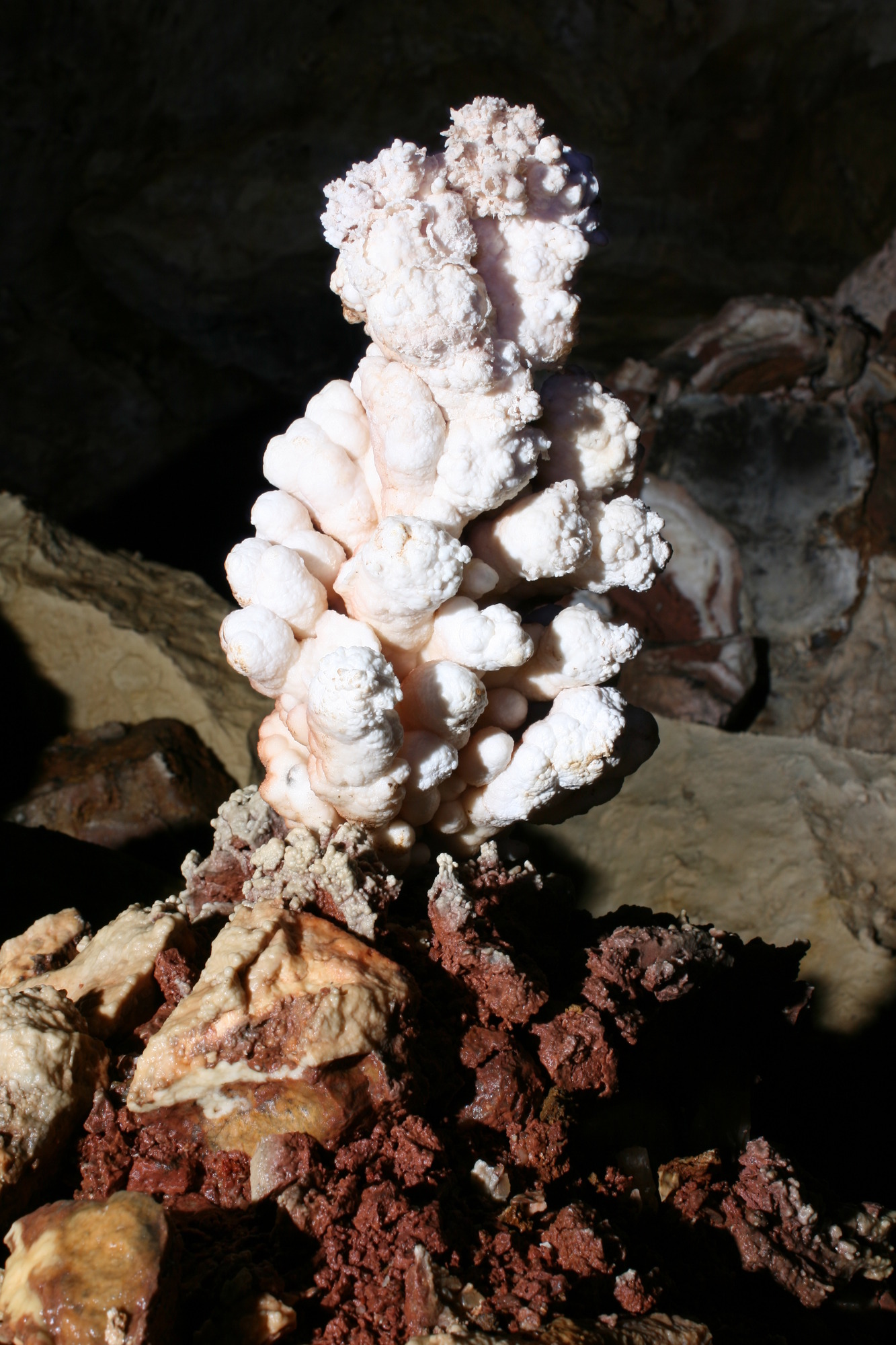 A bumpy calcite popcorn formation growing above red iron-rich paleofill