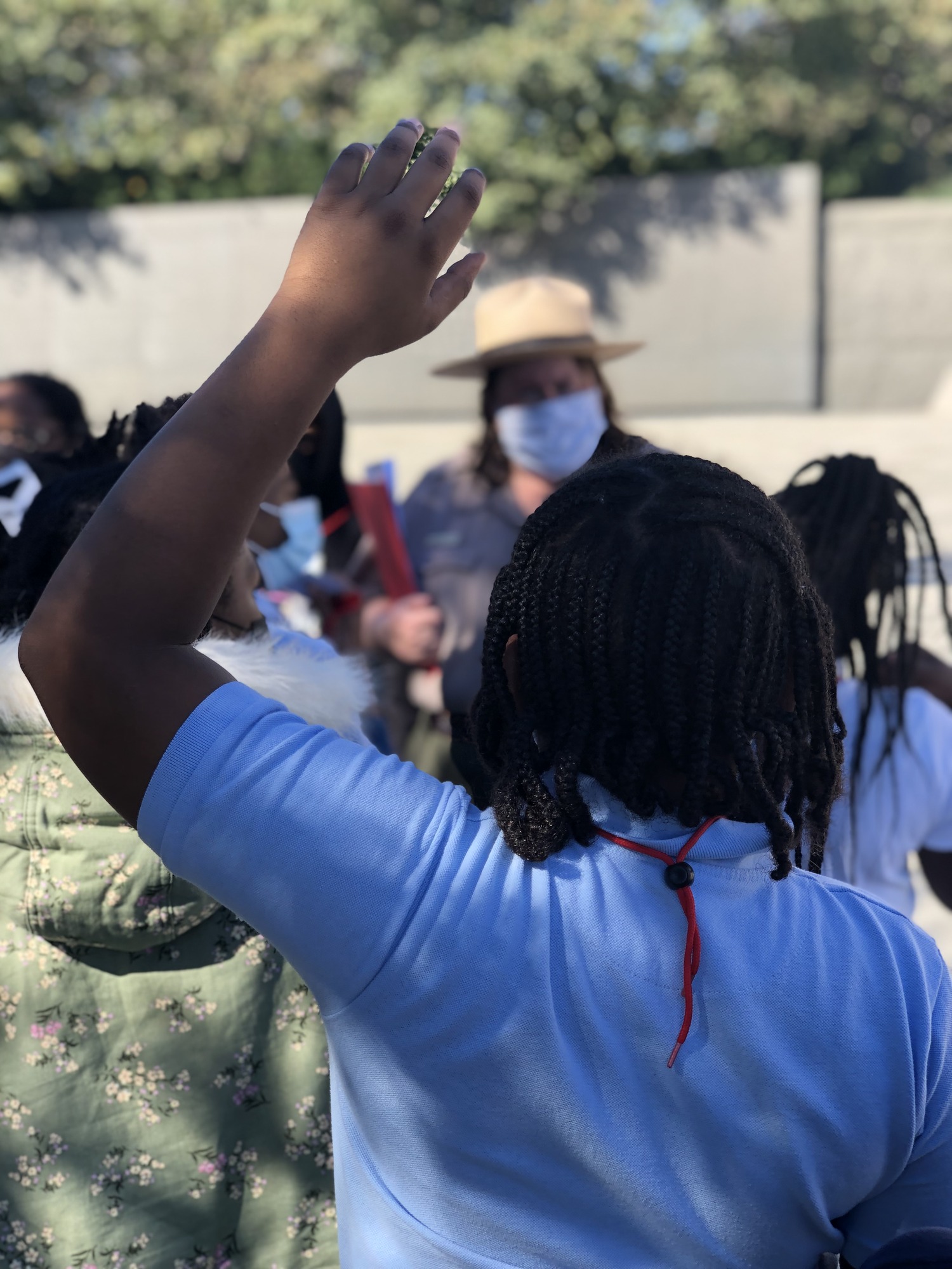 A student in the foreground raises their hand in response to a presentation given by a Park Ranger who is blurred in the background. 
