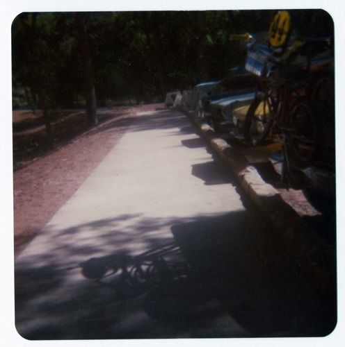 Completed sidewalk and parking area by the new Grotto footbridge. Cars and trucks parked along curb.
