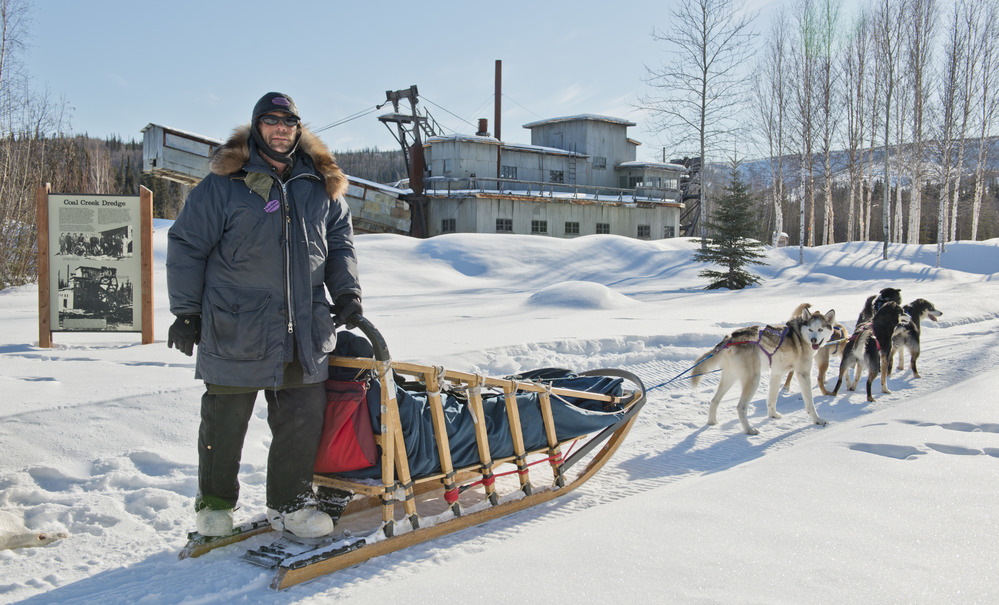 Wayne Hall of Bush Alaska Expeditions stands with his dogteam in front of the Coal Creek Dredge