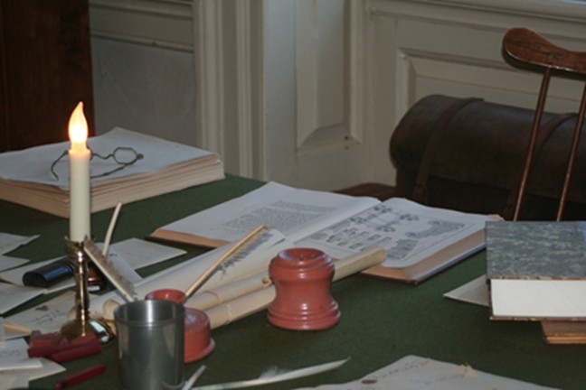 Desk with writing equipment and books located in the aide-de-camp office inside General George Washington's Headquarters.
