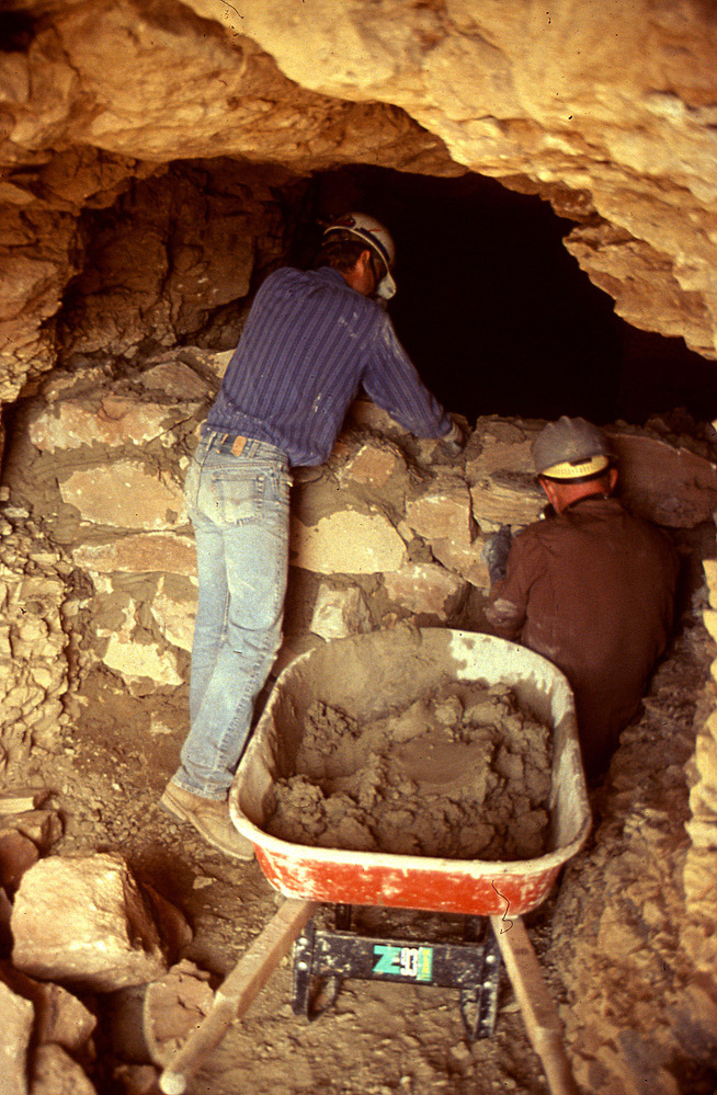 Workers building a stone and masonry wall in a mine entrance.