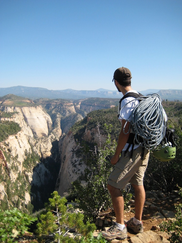 A man with a rope on his back overlooks a deep canyon. 