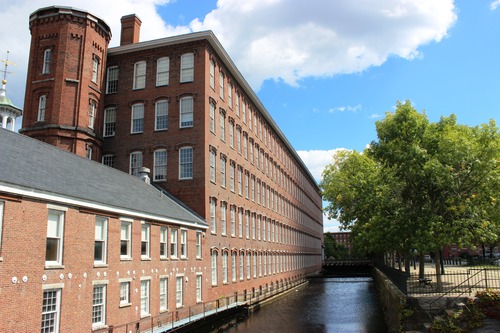 A canal flows by a five story brick mill building