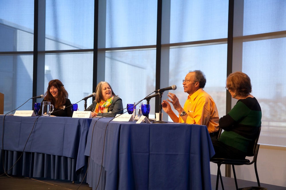 Four people site at a table on stage talking into microphones. 