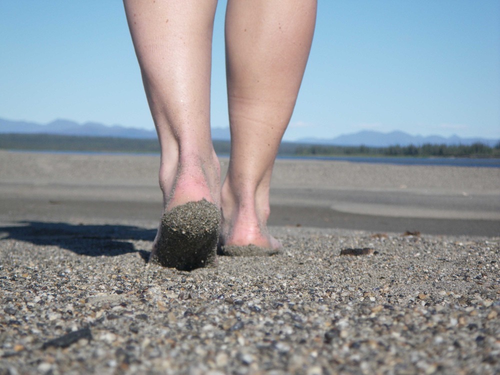 Close image of bare feet walking away across the sand.
