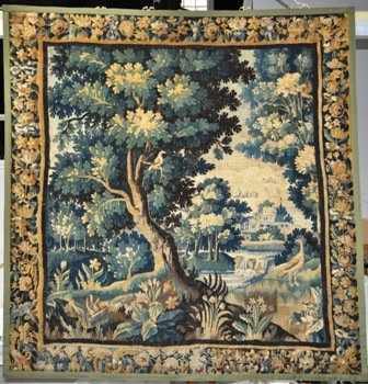 A wall tapestry with house, trees and animals.