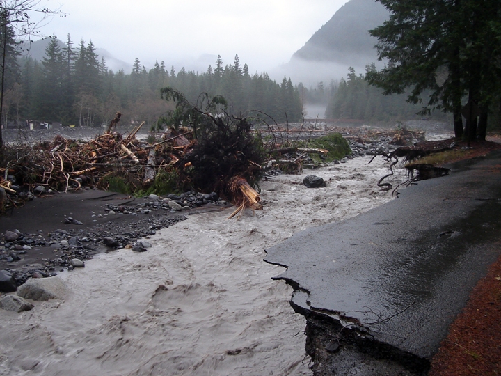A raging muddy river flows under the edges of an undercut paved road. 
