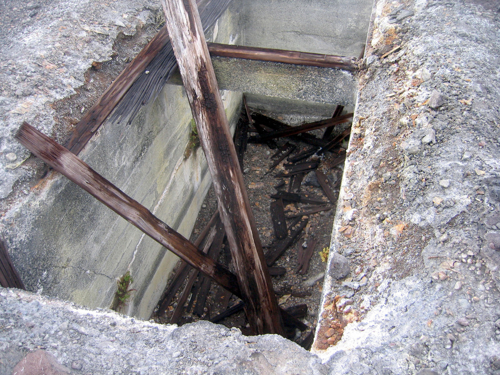 A rectangular concrete vault with pieces of timber framing opens into the ground. 