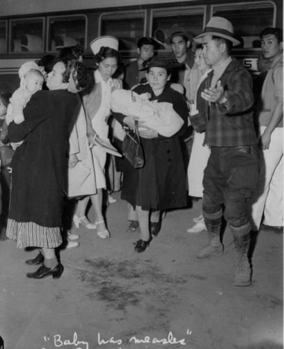 Before disembarking from bus at War Relocation Center, evacuees of Japanese descent are again examined by fellow evacuee medical staff. This baby (center) was found to have measles. The nurse is accompanying mother and child to Manzanar hospital.