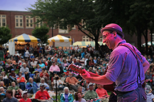  A man, with his back to us, plays a guitar in front of a large crowd looking at him, at the Lowell Folk Festival
