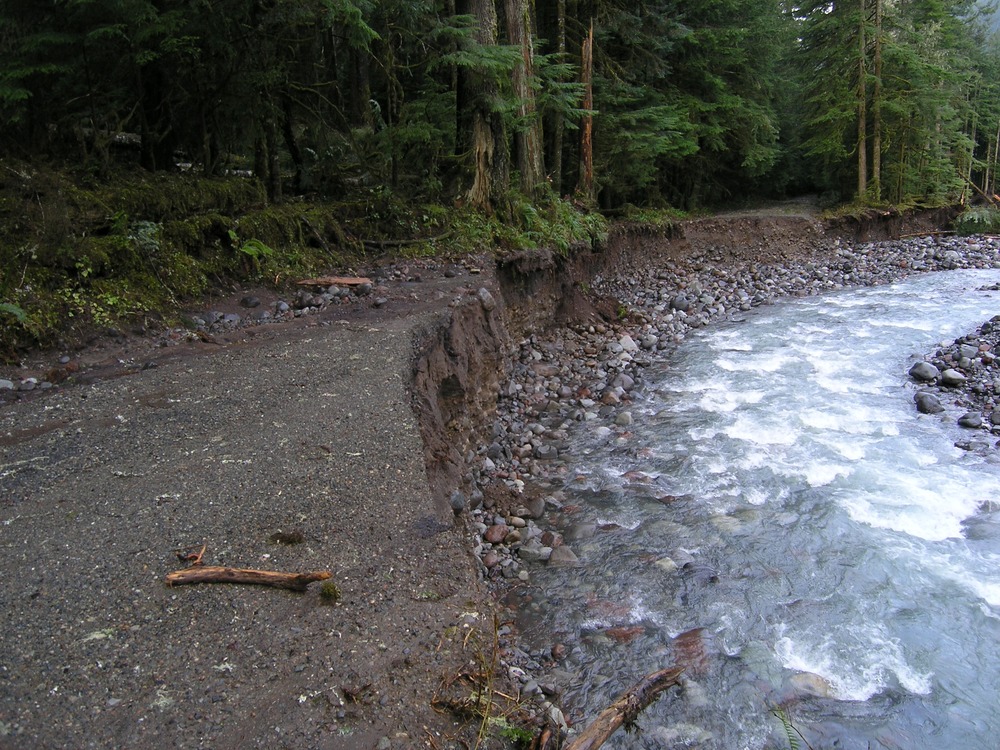 A river carves out a large section of a road. 