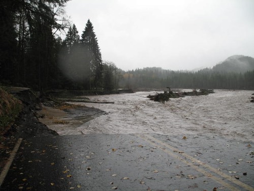 The pavement of a road abruptly ends with a view of a wide muddy, flooded river. 
