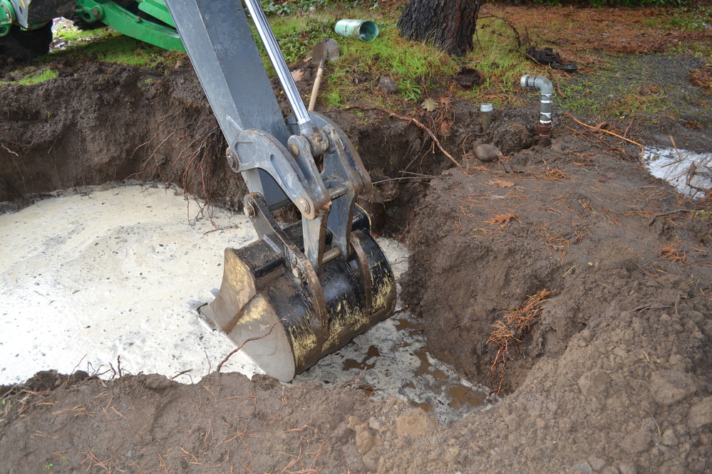 Image of a backhoe shovel above a hole filled with leaking water