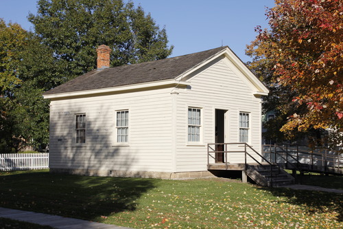 A one-story wooden building painted off-white with two windows and a central doorway.