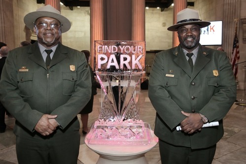 An ice sculpture encourages visitors to Find Your Park while two Park Rangers flank the sculpture.