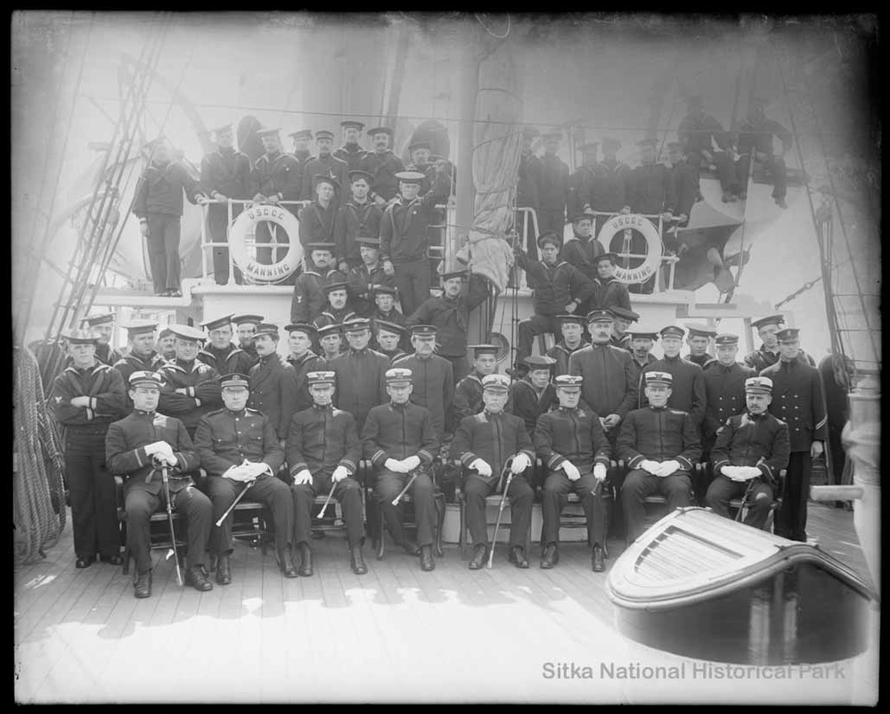 Officers and crew of a US Coast Guard ship posing for the photo on deck of the ship.