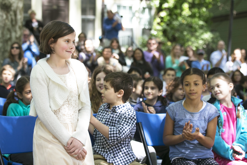A girl in a white dress stands as she is announced an essay winner