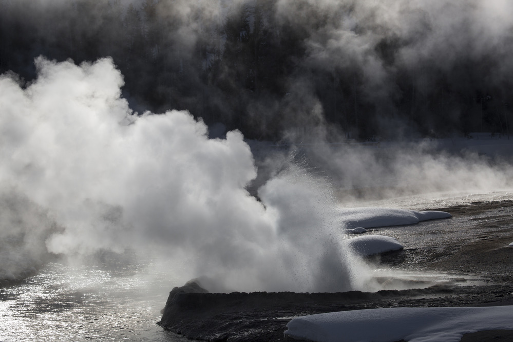Cliff Geyser at Black Sand Basin erupts next to the Firehole River in low light.