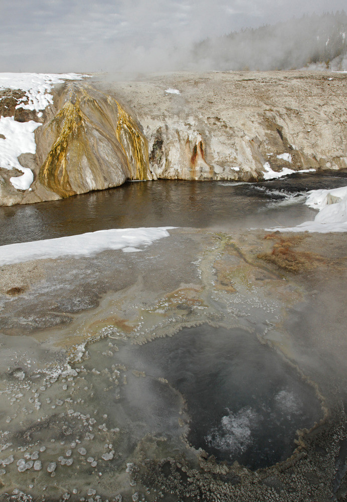 Looking across the top of a bubbling hot spring and a river at heated runoff water flowing down the bank to the river.
