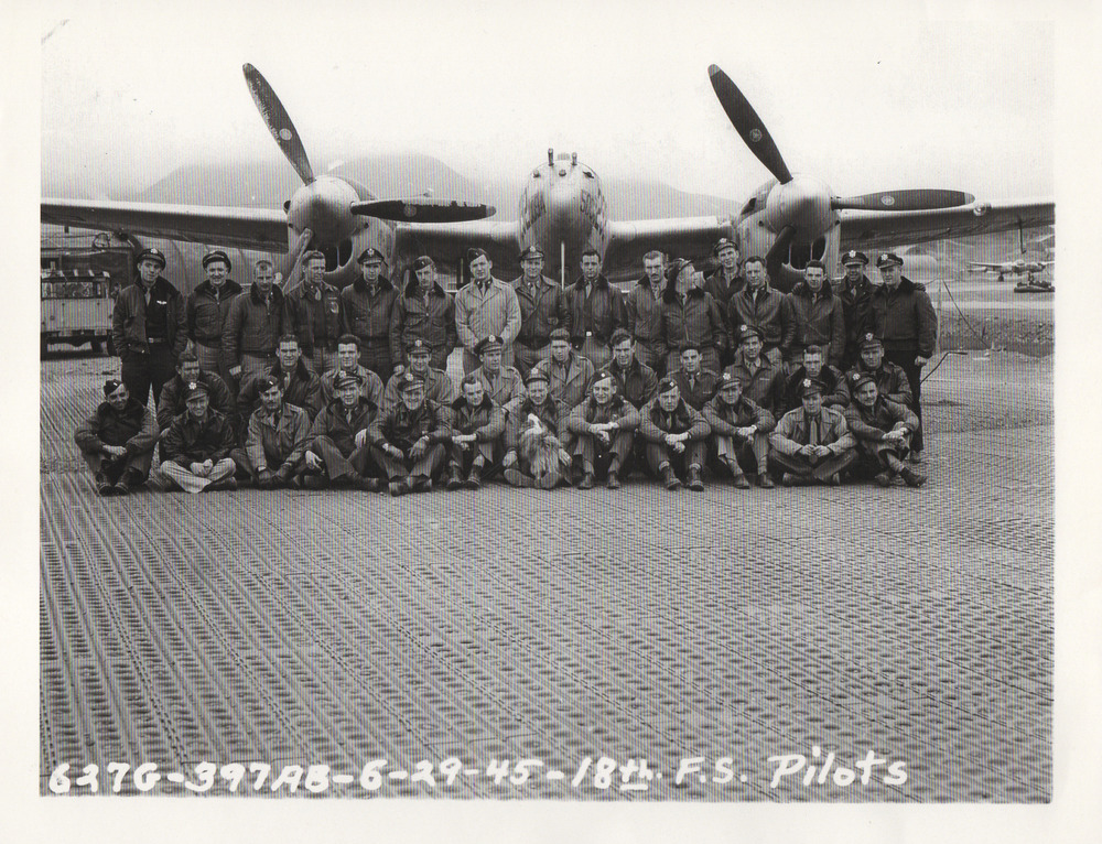 Black and white photo of three rows of men and one dog posing in front of a prop plane.