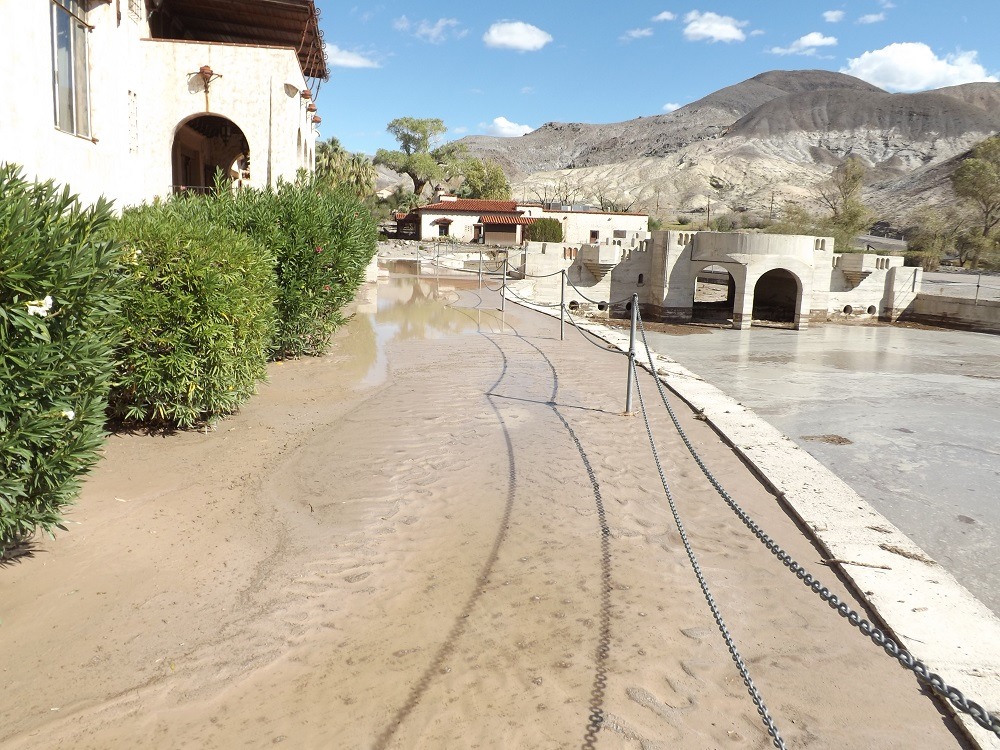 a muddy walkway next to a large swimming pool filled with mud and water
