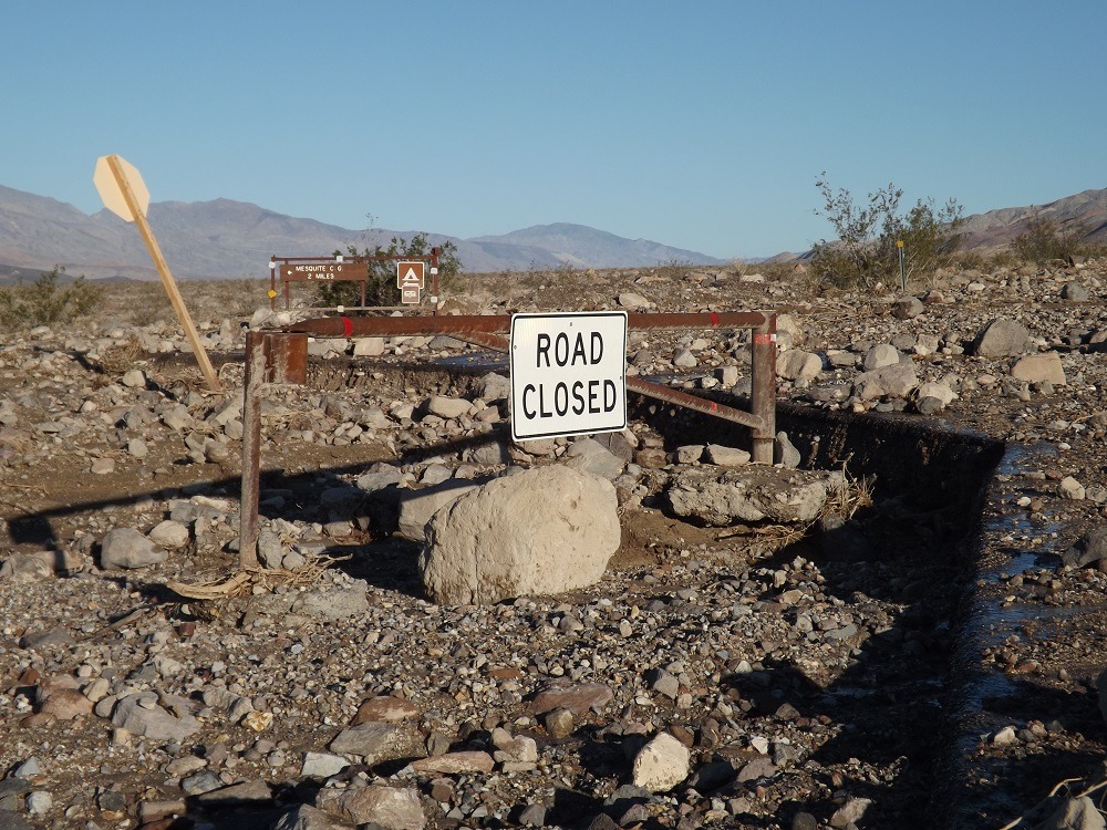 a "road closed" sign on a barricade among mud, rocks, and boulders