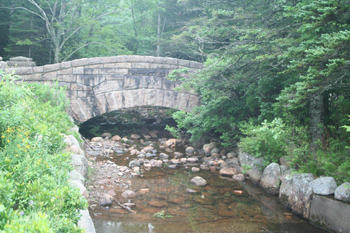 A stone bridge arches over a shallow waterway, flowing through a stone-lined channel 