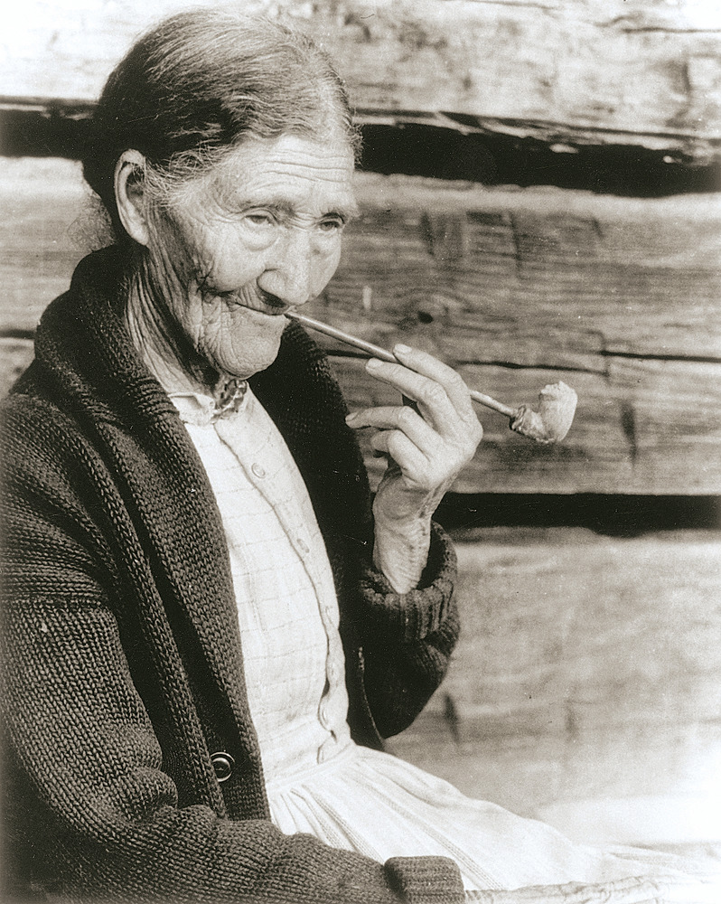 Historic photo of an eldery woman smoking a clay pipe