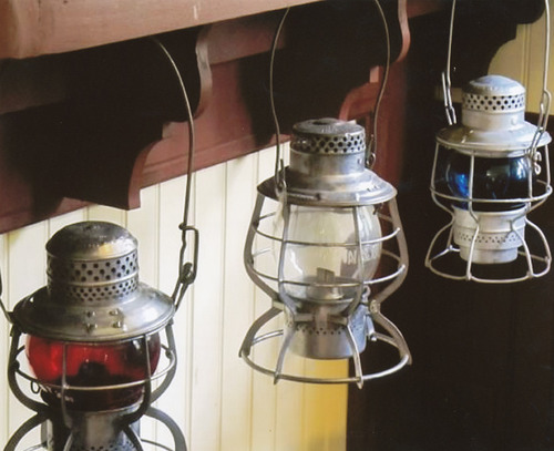 three old railroad lanterns hanging under a shelf