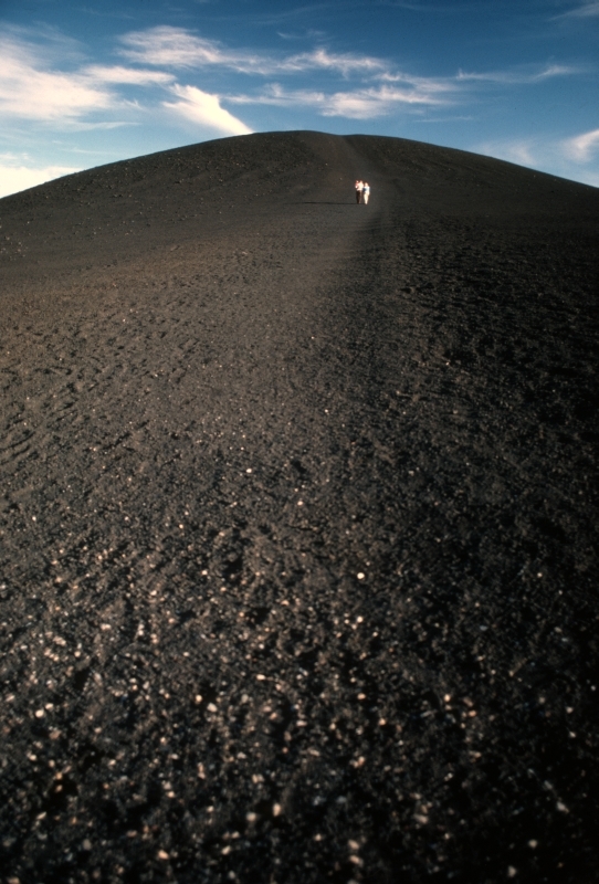 visitor climbing a bare, black cinder cone